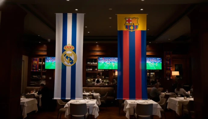 Decoración elegante de un restaurante temático de fútbol con banderas gigantes del Real Madrid y FC Barcelona colgando del techo frente a las mesas.